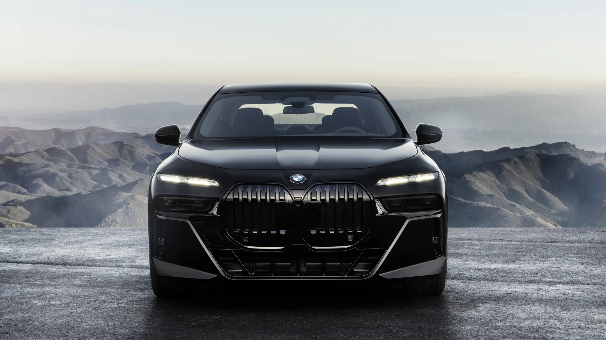 A dark premium saloon photographed head-on against a mountain landscape